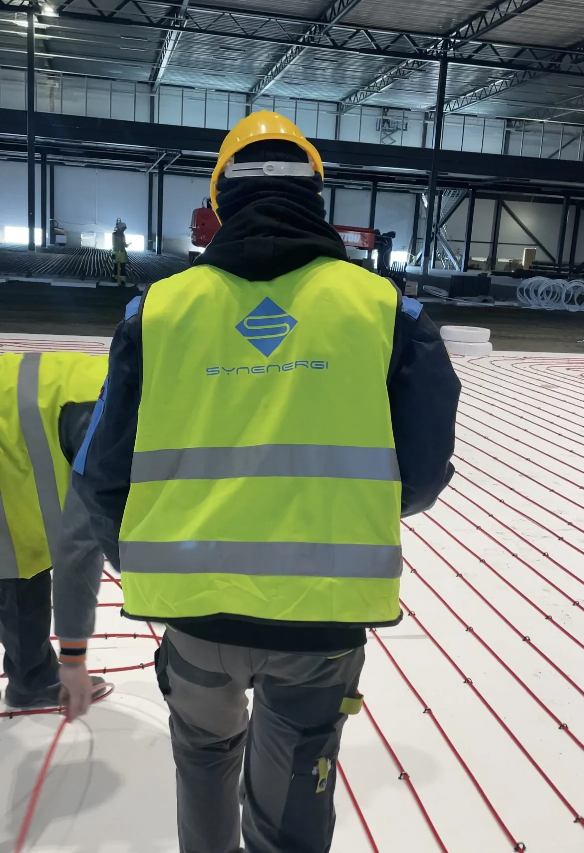 Installers in high-visibility vests on a floor covered with red heating pipes